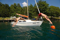 Couple jumping from a sailing boat into Millstätter See (deepest lake of Carinthia), Millstatt, Carinthia, Austria