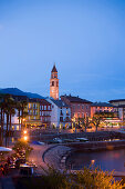 Harbour and harbour promenade with spire of church Santi Pietro Paolo in background in the evening, Ascona, Lake Maggiore, Ticino, Switzerland