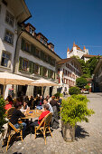 People sitting in pavement cafe of restaurant Ratsstübli, Rathausplatz (town hall square), Castle Thun in background, Thun (largest garrison town of Switzerland), Bernese Oberland (highlands), Canton of Bern, Switzerland