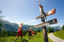 Three hikers walking past a sign post, Bichlalm 1731 m, Grossarl Valley, Salzburg, Austria