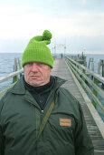 fisherman at the Baltic sea, Germany, portrait, people from germany, german, man with cap, man with pompom hat, pompom hat, green pompon hat, direct view, direct look in the camera, straight look in the camera, grim, a grimmer man, grimmer look, headgear,