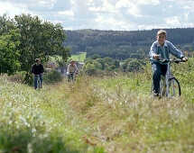 Junge, sportliche Familie mit Sohn, Fahrradtour auf einem Wiesenweg, im Hintergrund das Schloßhotel Münchhausen, bei Hameln, Weserbergland, Niedersachsen, Deutschland