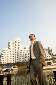 Young business man in front of modern office buildings, Neuer Zollhof, Architecture from Frank Gehry, Media Harbour Düsseldorf, state capital of NRW, North Rhine-Westphalia, Germany