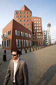 Young business man walking past Neuer Zollhof, modern architecture from Frank Gehry, Media Harbour, Düsseldorf, state capital of NRW, North-Rhine-Westphalia, Germany