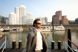 Young business man in front of modern architecture from Frank Gehry, office buildings, Media Harbour, Neuer Zollhof, Düsseldorf, state capital of NRW, North-Rhine-Westphalia, Germany