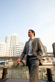 Young business man walking through Media Harbour, in front of modern architecture from Frank Gehry, office buildings, Düsseldorf, state capital of NRW, North-Rhine-Westphalia, Germany