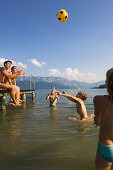 Family at lake Attersee, children standing in water playing with a ball, Salzkammergut, Upper Austria, Austria