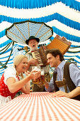 Couple clinking beer glasses in a beer tent, man playing melodeon in background