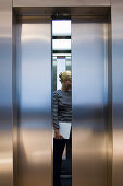 Junge Frau steht mit einem Laptop in einem Aufzug, Luxemburg