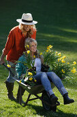 Young woman pushing friend sitting in hand barrow, Brannenburg, Upper Bavaria, Bavaria, Germany