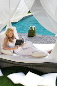 A young woman reading a book, resting on a sun lounger near the pool, near Uluwatu, Bali, Indonesia