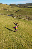 Girl running on farmland, grazing sheep, near Puponga, Golden Bay, northern coast of South Island, New Zealand