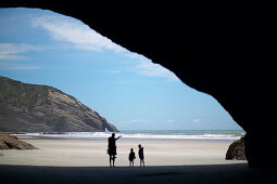 Family hiking, cave at Wharariki Beach, low tide, near Puponga, northwestern coast of South Island, New Zealand