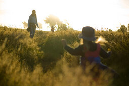 Mutter und Kind laufen durch hohes Gras, Sonnenuntergang an der Westküste, bei Haast, Südinsel, Neuseeland