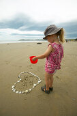 Mädchen findet Herz aus Muscheln am Strand, an Moeraki Boulders, südl. Oamaru,  Ostküste, Südinsel, Neuseeland