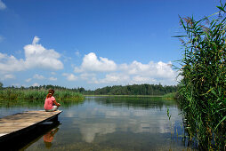 Frau sitzt auf einem Steg am Fohnsee, Osterseen, Oberbayern, Bayern, Deutschland