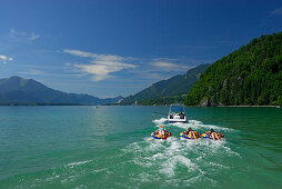 three young women tube riding behind motor boat, lake Abersee, lake Wolfgangsee, Salzkammergut, Salzburg, Austria