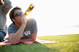 Man lying on blanket while drinking a bottle of beer, Ambach, Lake Starnberg, Bavaria, Germany