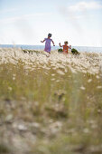 Boy and girl running through meadow of shore grass, Sysne, Gotland, Sweden