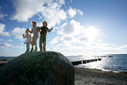 Three Kids standing on a big boulder, stone, on the beach, Torekov, Skane, Sweden
