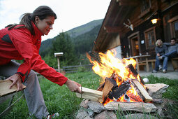 Frau legt Holz auf ein Lagerfeur, Heiligenblut, Nationalpark Hohe Tauern, Kärnten, Österreich