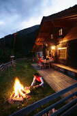 Junge Leute vor einer Almhütte, Lagerfeuer im Vordergrund, Heiligenblut, Nationalpark Hohe Tauern, Kärnten, Österreich