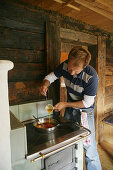 Mann kocht Rührei in einer Almhütte, Heiligenblut, Nationalpark Hohe Tauern, Kärnten, Österreich