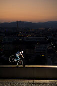 Trialbiker balanciert auf Kante von einem Hochhaus, Linz, Oberösterreich, Österreich