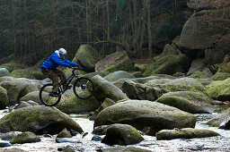 Trial biker on rocks of river, Muelviertel, Austria