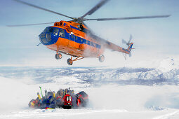 Helicopter picking up a group of skiers in snow, Heliskiing, Kamchatka Peninsula, Sibiria, Russia