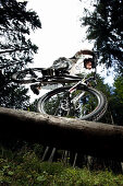 Junger Mann fährt Mountainbike auf einem Baumstamm, Oberammergau, Bayern, Deutschland