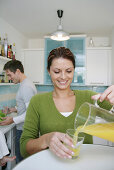 Young woman pouring a glass of juice, man in background, Munich, Germany