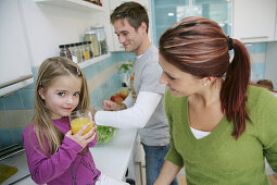 Family in kitchen, daughter drinking a glass of juice, Munich, Germany