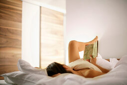 Junge Frau liegt im Bett und liest, Sand in Taufers, Südtirol, Italien