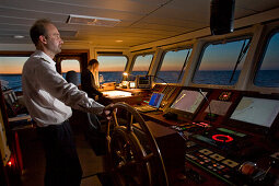 Captain at the helm and helmsman in training on the bridge of a ship, on the Hanse Explorer in the evening, Great Britain