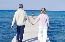 Father, mother and child walking in a wooden footbridge over the sea