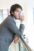 24 year old man standing against barrier serious expression, hand on chin