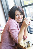 21 year old girl, sitting in bar, smiling at camera, holding a cup of coffee
