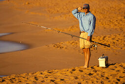 Surfcasting at Playa Solmar in early evening, beach, man hold fishing rod, tackle box on sand. Cabo San Lucas. Mexico