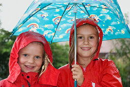 Zwei Mädchen (6-7 Jahre) in Regenkleidung unter einem Regenschirm, Oberbayern, Bayern, Deutschland