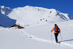 Female backcountry skier in Kleinwalsertal, alpine hut in background, Allgaeu Alps, Vorarlberg, Austria