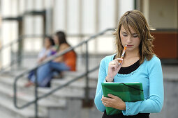  Aktivität, Außen, Eine Person, Eins, Erziehung, Farbe, Fokus, Halbfigur, Jugend, Jung, Mädchen, Mensch, Menschen, Nachdenklich, Stehen, Stehend, Student, Studenten, Studie, Studieren, Studium, Tageszeit, Teenager, Weiblich, L43-466624, agefotostock 