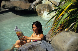 Young woman reading a journal in the hot springs of Hanmer Springs, South Island, New Zealand