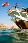Frau springt vom Boot ins Wasser, Boot mit Touristen, Dhau, Haijar Gebirge, Musandam, Oman