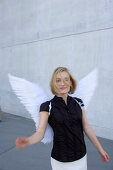 Mid adult woman wearing angel wings near a concrete wall