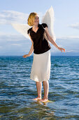 Mid adult woman wearing angel wings standing in lake Starnberg, Bavaria, Germany