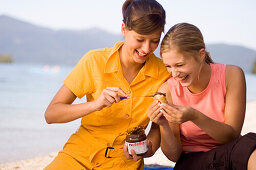 Two young women, girls, having a picnic on the lake shore, eating Nutella, Lake Walchensee, Upper Bavaria, Bavaria, Germany