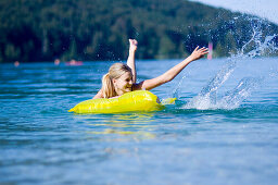 Young woman on an airbed on lake Walchensee splashing with water, Bavaria, Germany