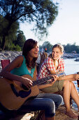 Two young women sitting at river Isar in the evening, Munich, Bavaria, Germany