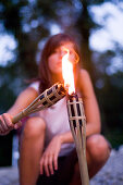 Young woman lighting a torch on the banks of the river Isar in the evening, Munich, Bavaria, Germany